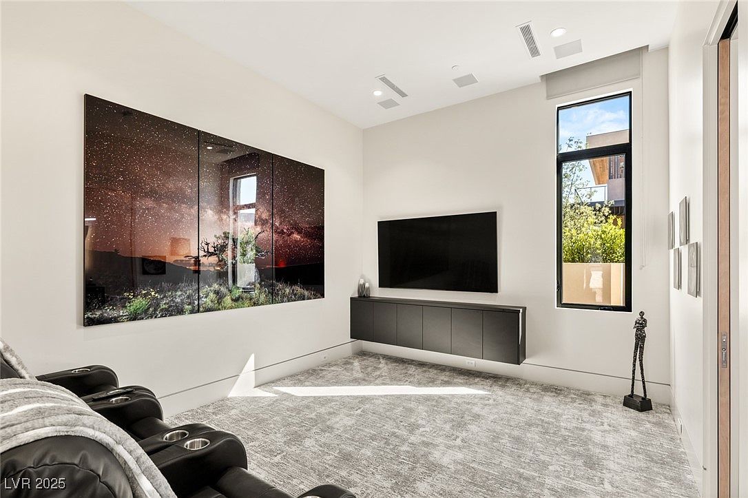 This interior shot showcases a modern living room with a large, multi-panel artwork depicting a starry night landscape. A sleek, wall-mounted entertainment unit sits beneath a flat-screen TV, and a tall window provides natural light. The room features comfortable seating and a neutral color palette, creating a sophisticated and inviting atmosphere.