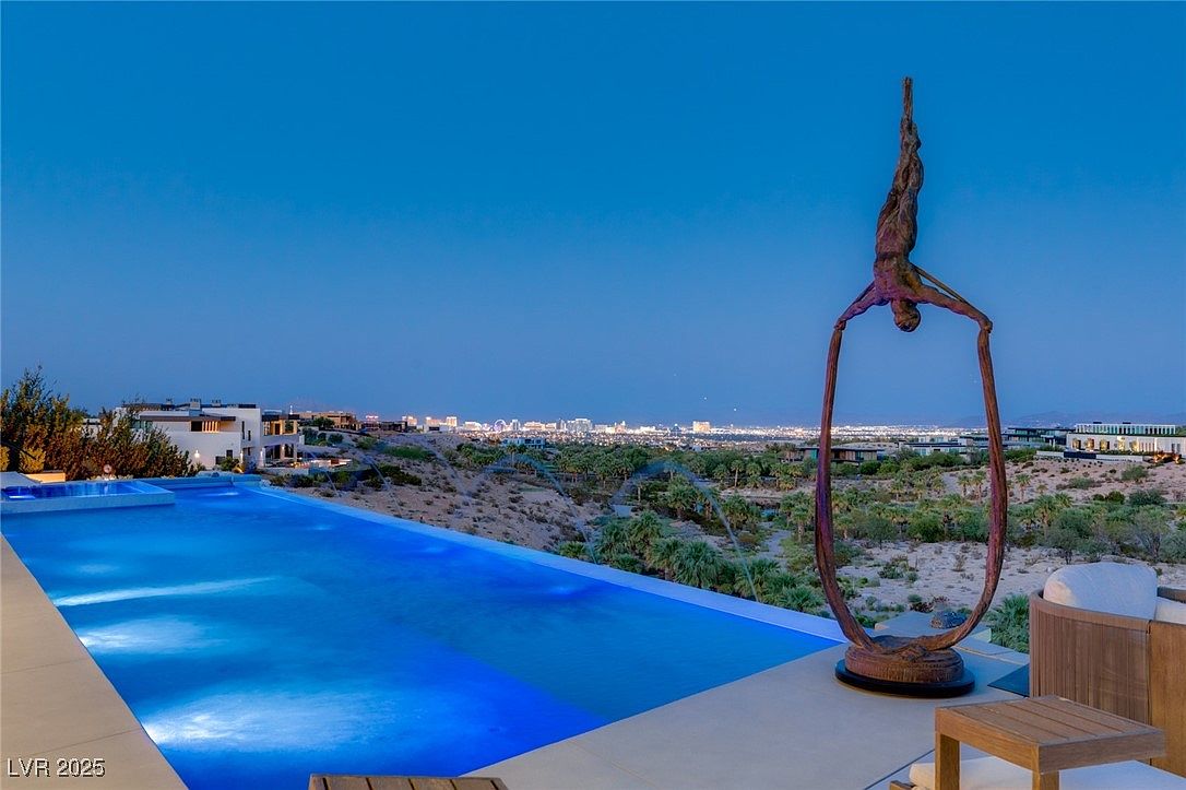 This image showcases a luxurious infinity pool with a stunning view of the city skyline at dusk. A modern sculpture stands elegantly beside the pool, adding an artistic touch to the outdoor space. The pool's blue water contrasts beautifully with the surrounding landscape, creating a serene and upscale ambiance.