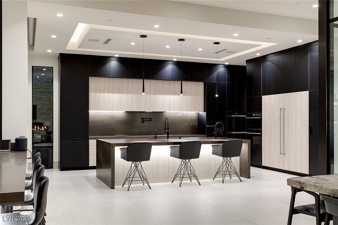 This is a modern kitchen with a large island featuring seating and pendant lighting. The cabinetry is a mix of dark and light wood tones, creating a sophisticated contrast. The kitchen is well-lit with recessed lighting and features high-end appliances, contributing to a luxurious and functional space.