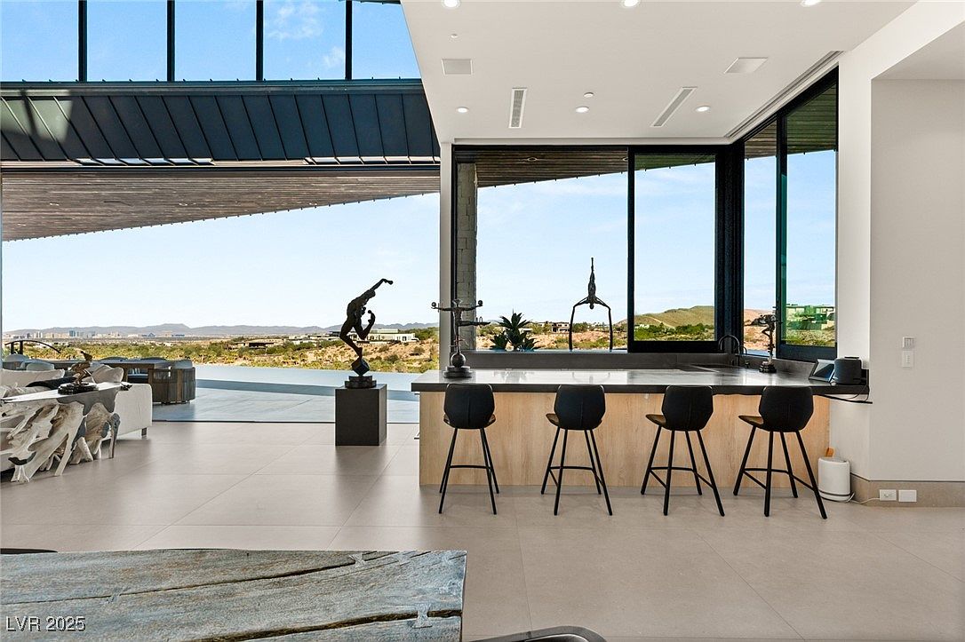 This interior shot showcases a modern kitchen with sleek countertops and bar seating. Large windows offer expansive views of the landscape, seamlessly blending indoor and outdoor spaces. The open floor plan and minimalist design create a sophisticated and airy atmosphere.
