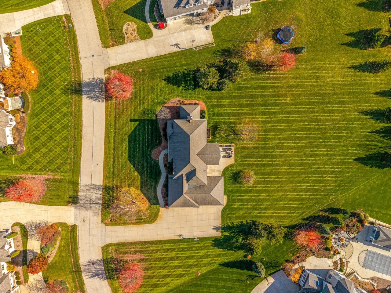 This is an aerial view of a large, well-manicured property. The home features a complex roofline and a spacious driveway. The yard is expansive with meticulously maintained lawn, mature trees, and landscaping, creating a park-like setting.