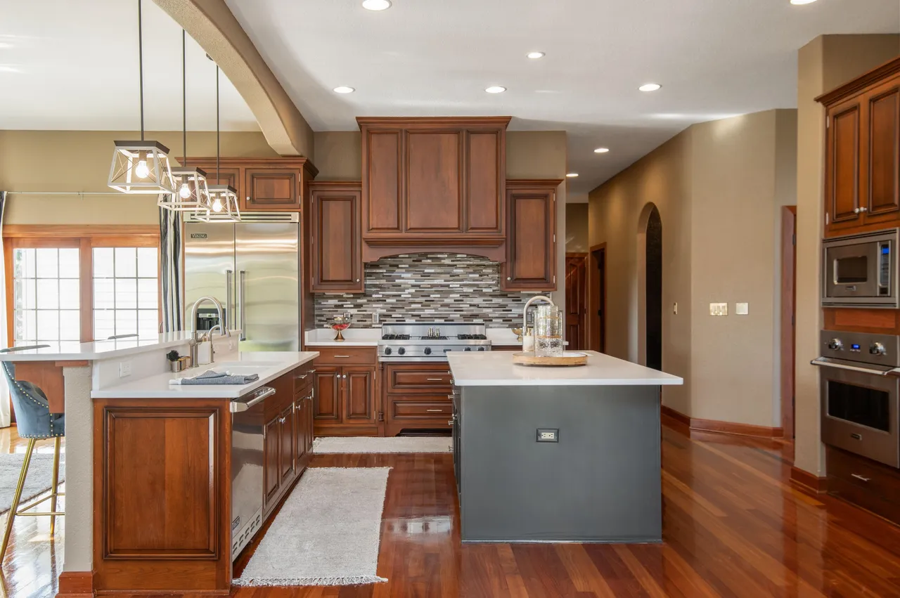 This spacious kitchen features dark wood cabinetry and a gray island with a white countertop. Stainless steel appliances, including a Viking refrigerator and double ovens, add a luxurious touch. The hardwood flooring and ample natural light create a warm and inviting atmosphere.