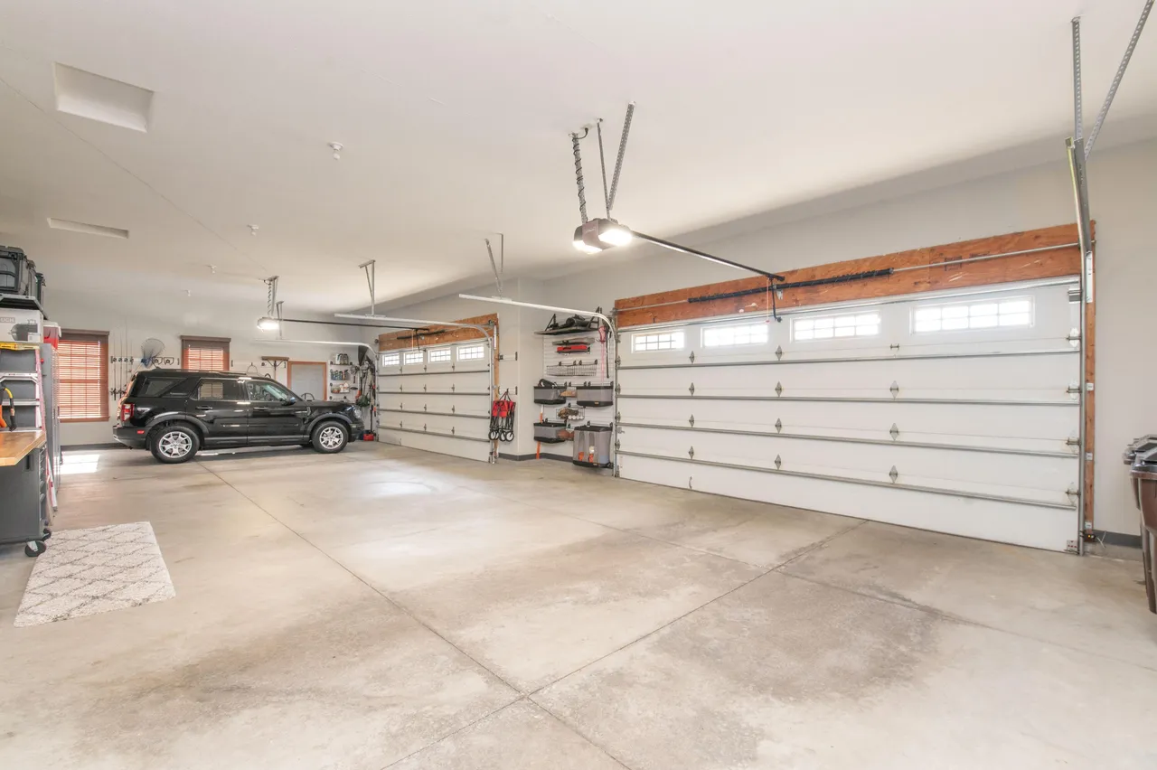 This is a spacious garage with three bays, each featuring a white sectional garage door with windows. The garage has a clean and well-maintained concrete floor, with ample space for parking and storage. Garage door openers hang from the ceiling providing automated access.