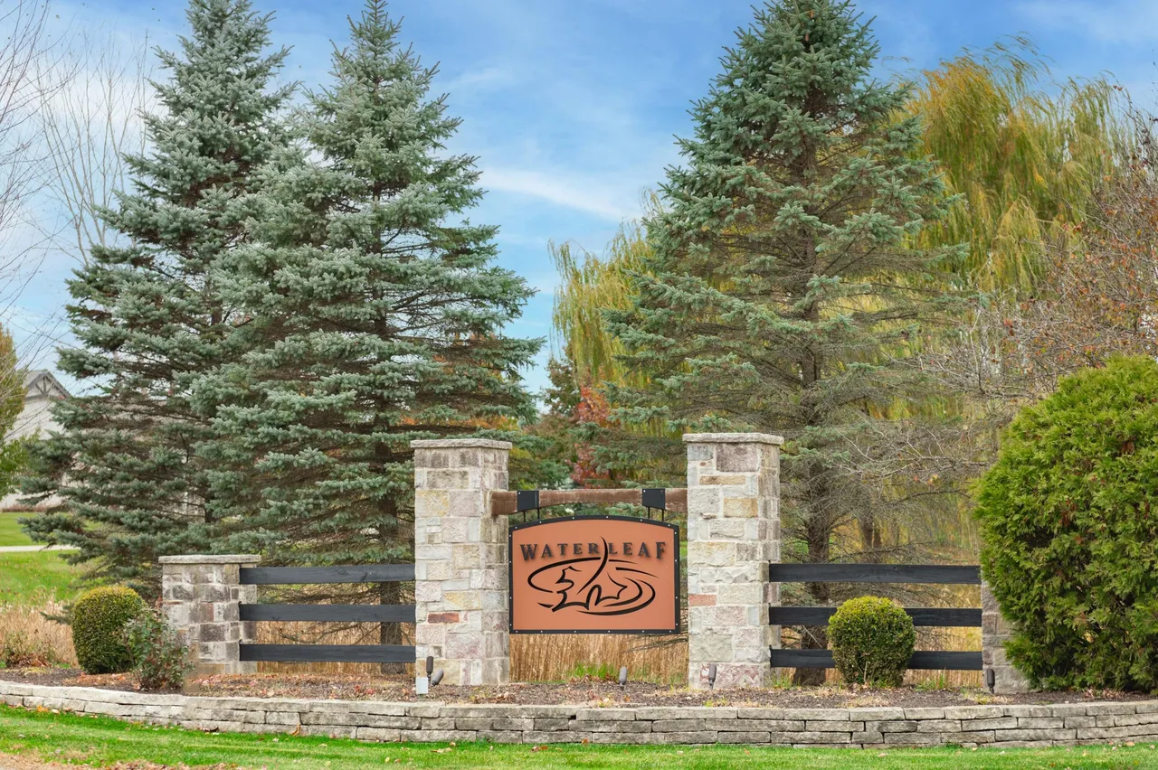 The image showcases the entrance sign for "Waterleaf," a residential community. The sign is constructed from stone pillars, a wrought iron gate, and a decorative nameplate. Landscaping including shrubs and trees surrounds the entrance, providing a welcoming and upscale impression.