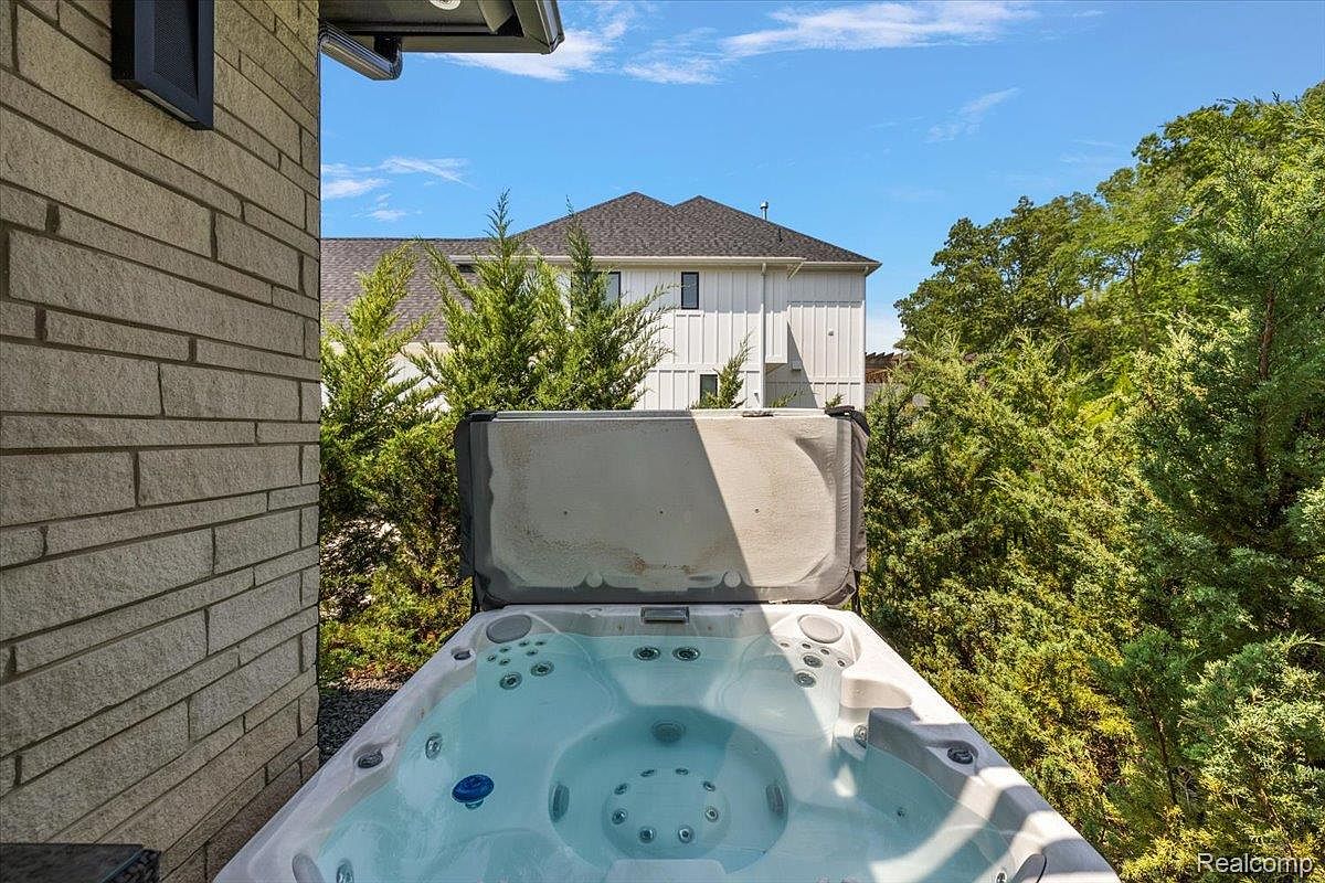 This image showcases a luxurious outdoor spa area, featuring a modern hot tub filled with clear water. The spa is surrounded by lush greenery, providing privacy and a serene atmosphere. In the background, a glimpse of the house's exterior can be seen, suggesting a well-maintained and upscale property.