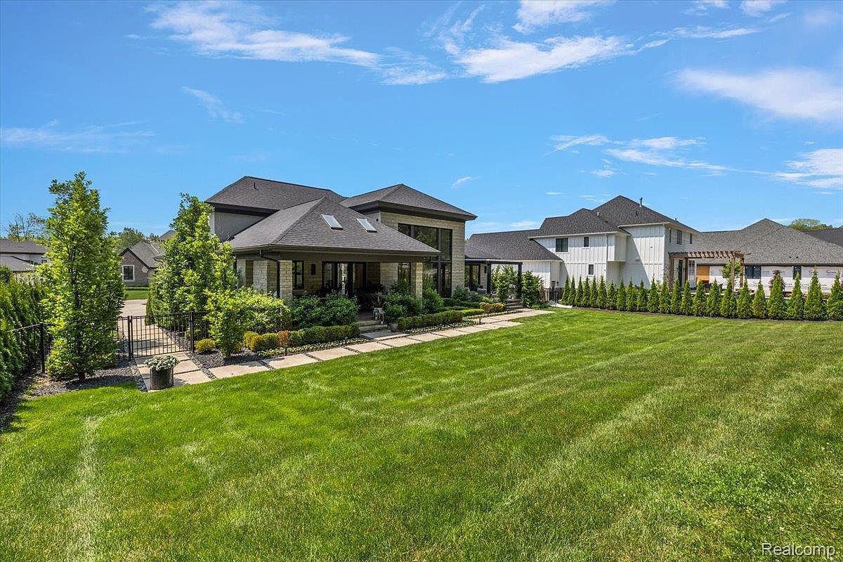 This image showcases a beautifully landscaped yard featuring a lush green lawn, manicured hedges, and mature trees. The modern home in the background has a covered patio area, adding to the outdoor living space. The overall impression is one of a well-maintained and inviting property.