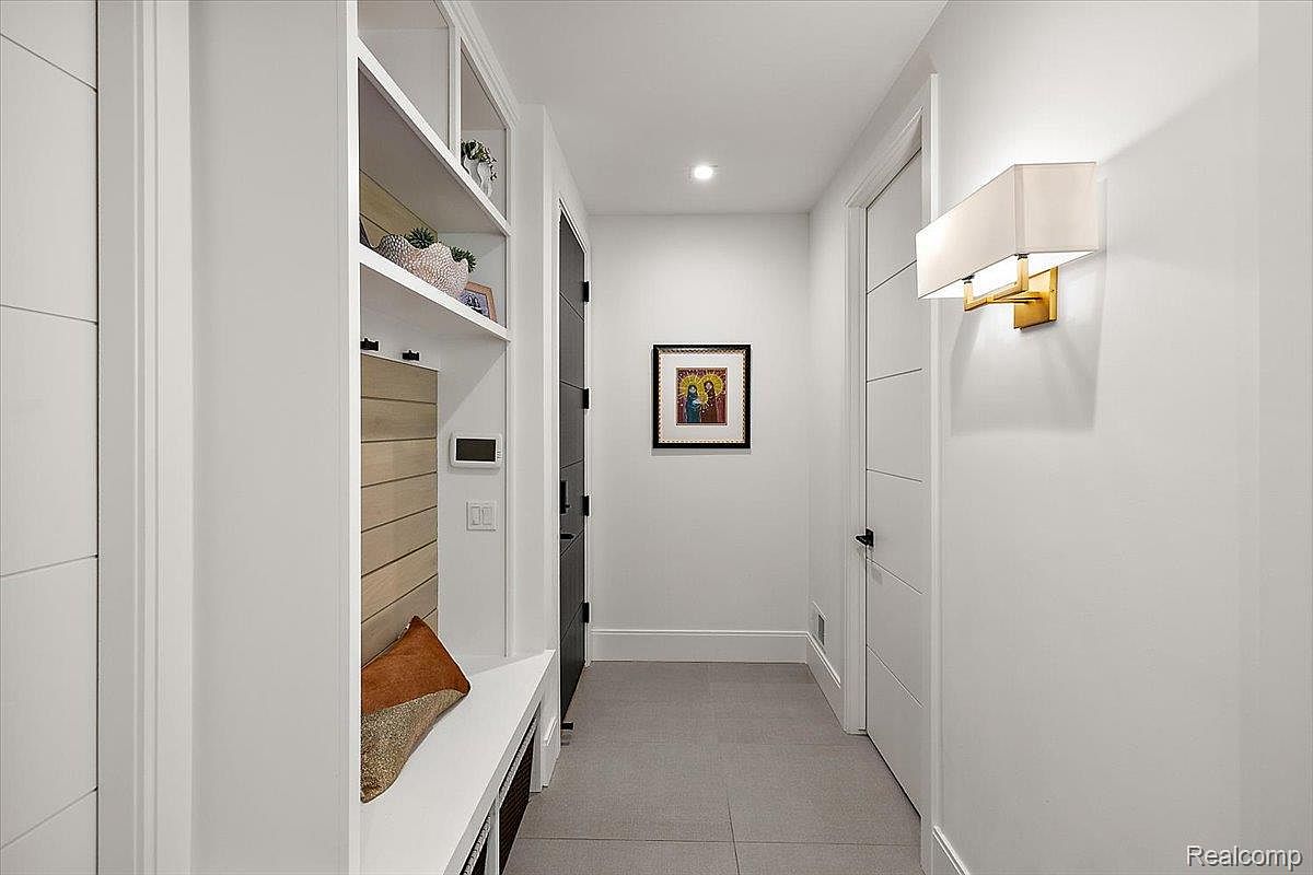 This is an interior shot of a modern hallway. The hallway features a built-in bench with shelving above, a framed picture on the wall, and a contemporary light fixture. The color palette is primarily white and gray, creating a clean and minimalist aesthetic.