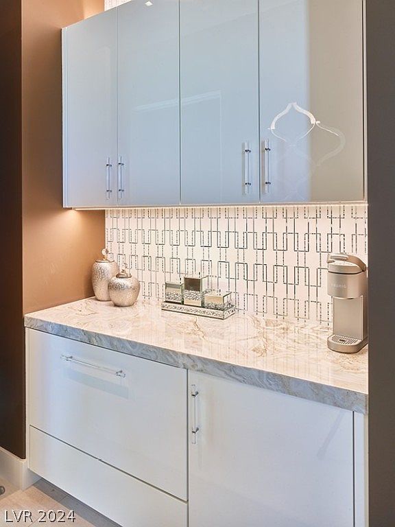 This is a detailed interior shot of a modern pantry area. The pantry features sleek, white cabinetry with long, clear handles, complemented by a light-colored countertop with subtle veining. A decorative backsplash adds visual interest, and the overall impression is clean and organized.