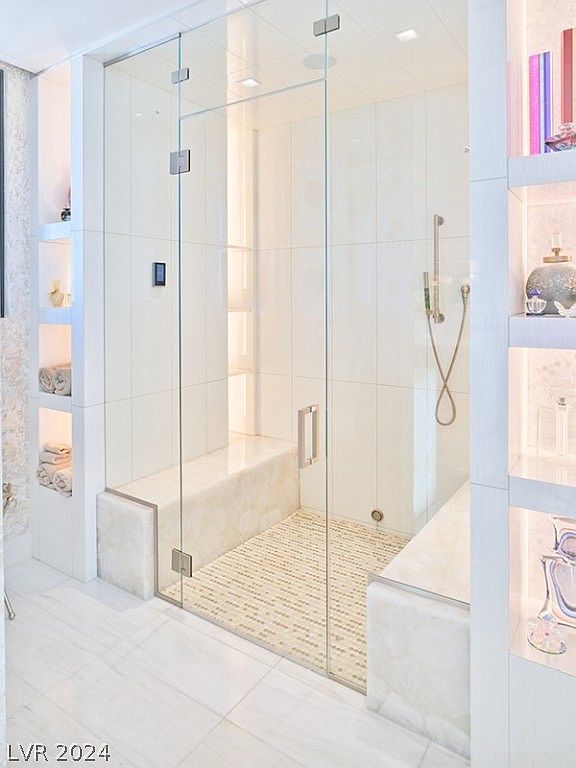 This is a luxurious primary bathroom featuring a glass-enclosed shower with built-in seating and a mosaic tile floor. The shower has a modern shower head and sleek hardware. Adjacent to the shower are built-in shelves with decorative items and towels, adding to the spa-like ambiance.