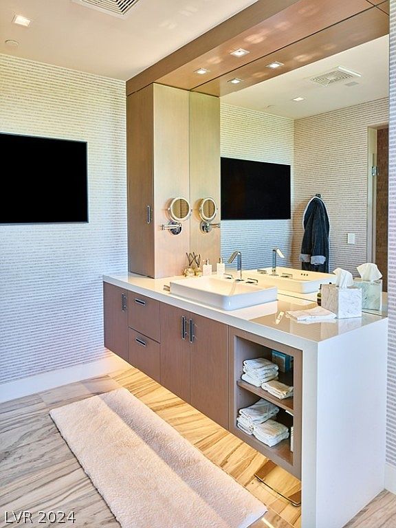 This is a modern primary bathroom featuring a floating vanity with light wood cabinets and a white countertop. A large mirror spans the length of the vanity, reflecting the space and enhancing the sense of openness. The flooring is a light-colored marble, and a plush rug adds warmth to the room.