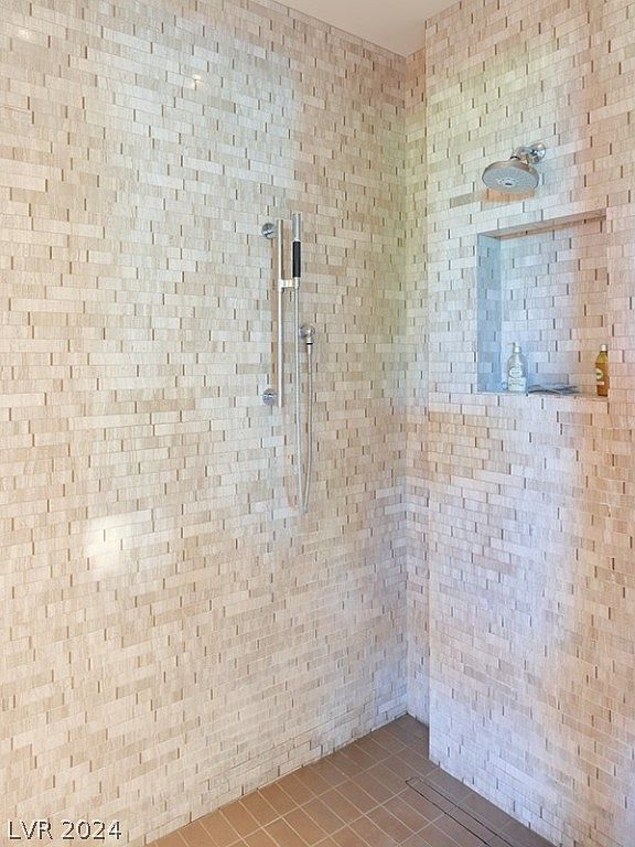 This is a well-lit primary bathroom showcasing a modern shower. The shower features a mosaic tile wall, a rainfall showerhead, and a built-in niche for toiletries. The floor is tiled, and the overall design is clean and contemporary, creating a spa-like atmosphere.