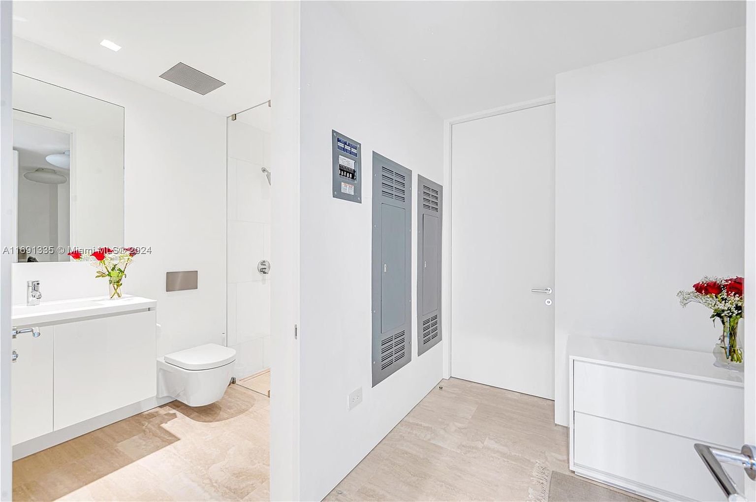 This is a bright and modern guest bathroom. It features a white vanity with a sleek countertop, a toilet, and a glass-enclosed shower. The walls are painted white, and the floor is tiled with a light-colored stone, creating a clean and airy atmosphere.