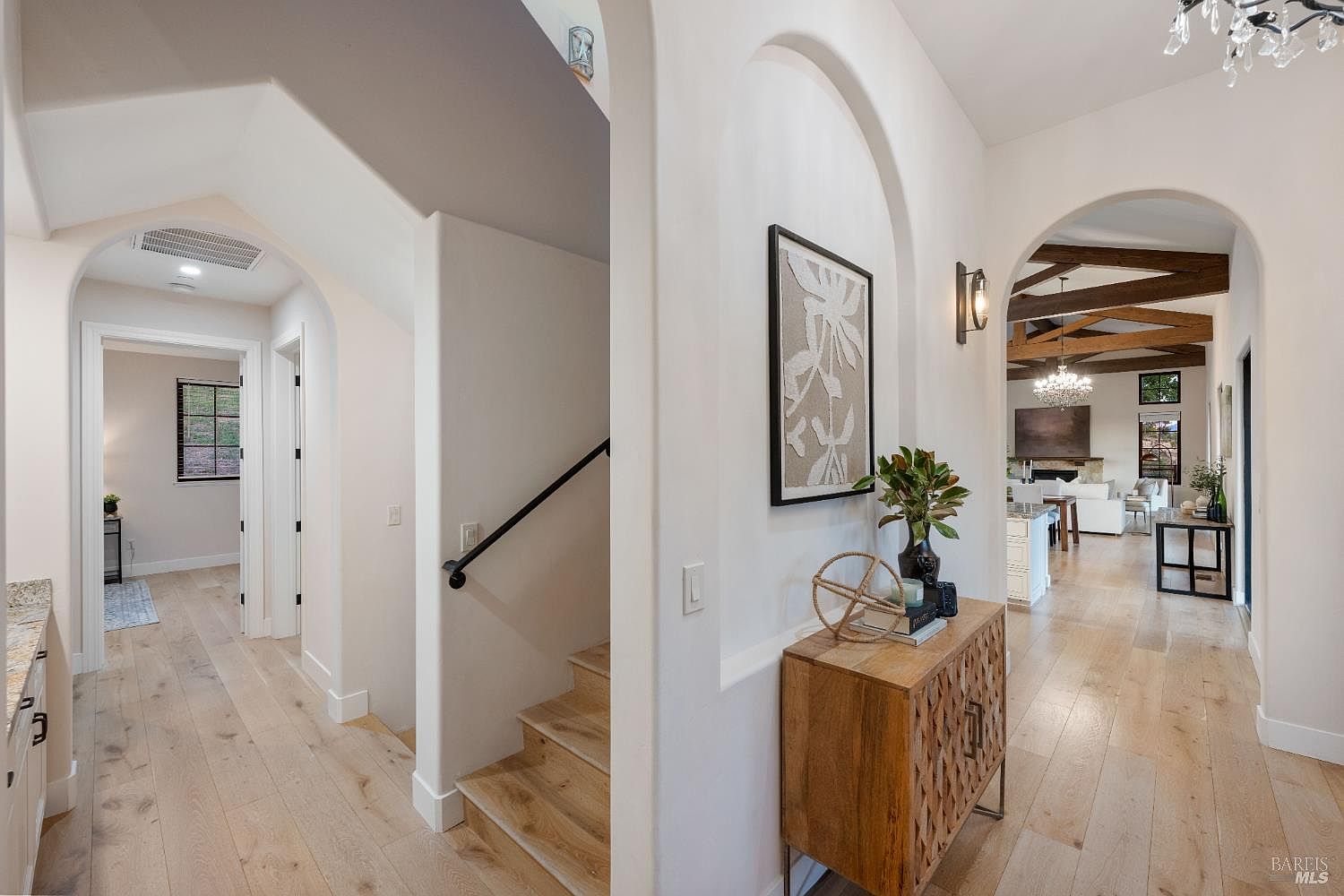 This interior shot showcases a bright and inviting hallway with light wood flooring and white walls, creating a clean and spacious feel. Arched doorways lead to other rooms, offering glimpses of the home's interior, including a living area with exposed wooden beams. A wooden console table with decorative items adds a touch of elegance to the hallway.