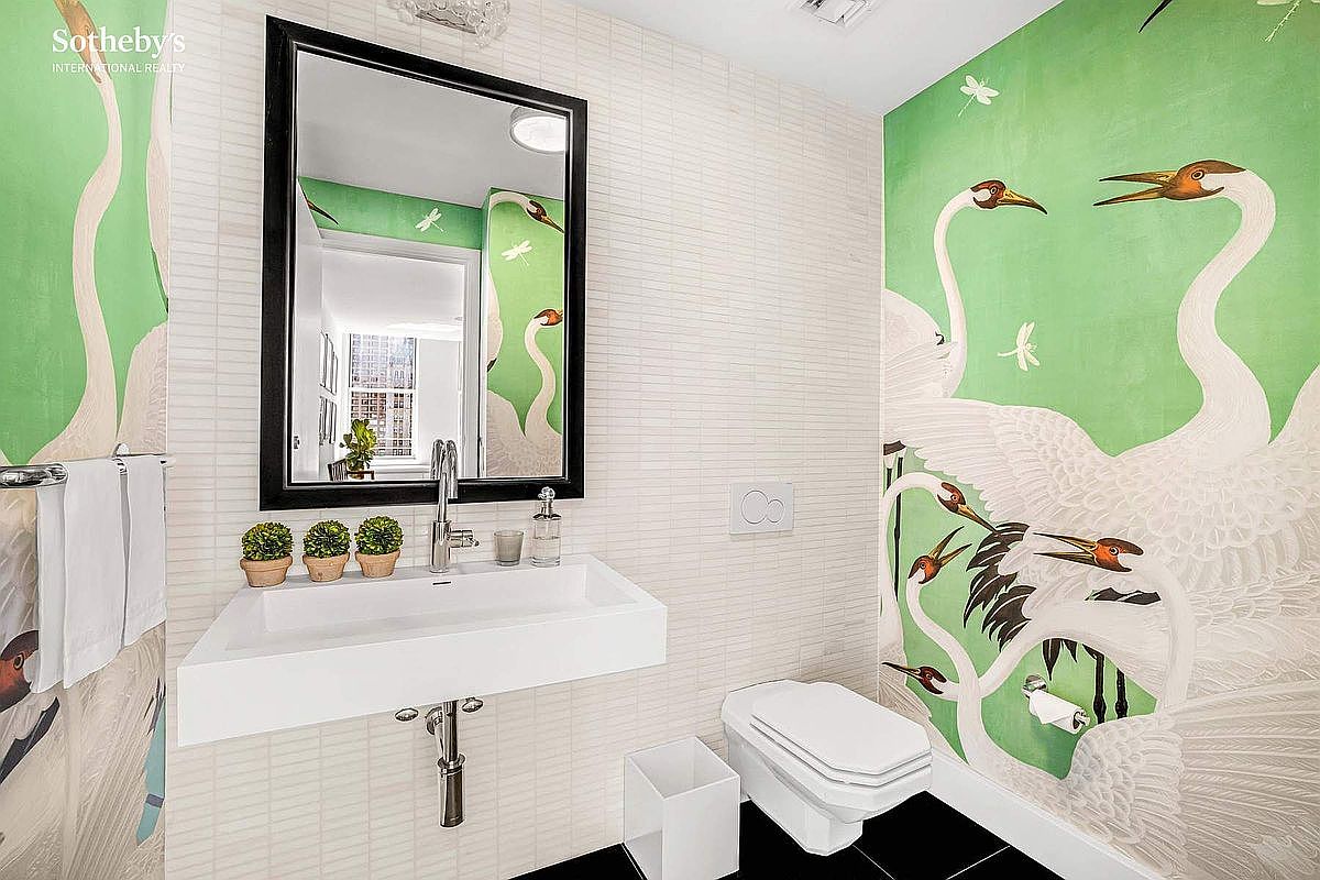 This is a stylish guest bathroom featuring a modern, wall-mounted sink with a sleek faucet and a black-framed mirror above. The walls are adorned with a combination of white horizontal tiles and a vibrant green wallpaper with a swan and dragonfly motif. Black flooring adds a touch of sophistication, and the overall impression is clean, contemporary, and artistic.