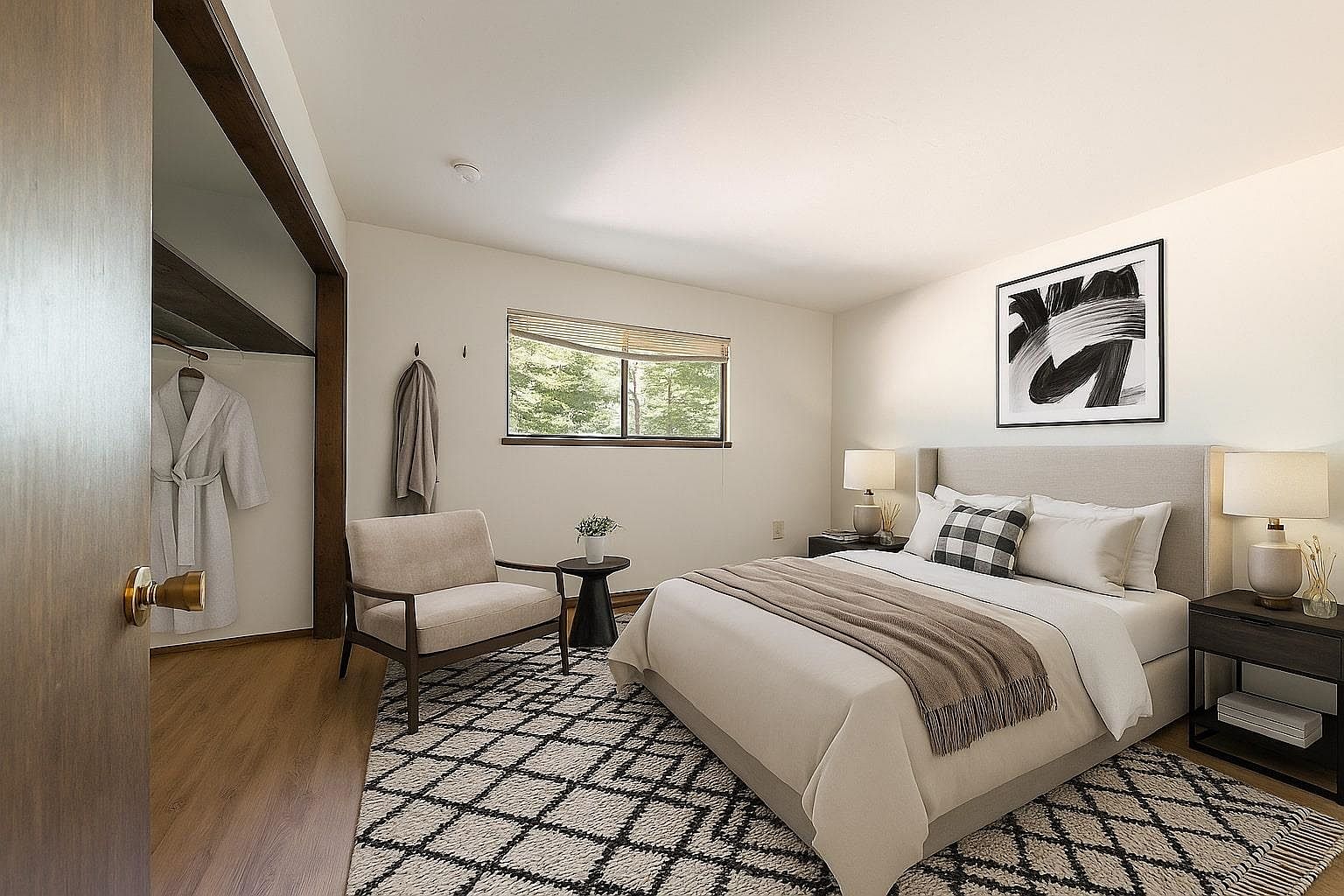 This is a cozy primary bedroom featuring a neutral color palette and a comfortable aesthetic. The room includes a bed with a light-colored headboard, a patterned rug, and a window providing natural light. A small seating area with a chair and side table adds to the room's functionality and charm, while artwork on the wall completes the space.