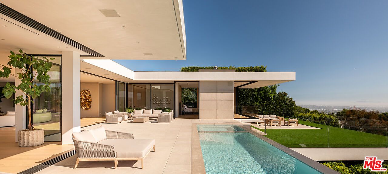 This image showcases a luxurious outdoor living space with a modern architectural design. A sleek infinity pool extends towards a manicured lawn and offers stunning views of the surrounding landscape. The patio area features stylish outdoor furniture, creating an inviting space for relaxation and entertainment.
