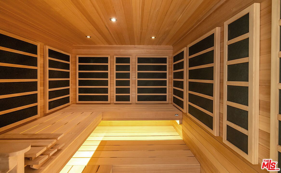 This is an interior shot of a sauna, featuring wooden walls, ceiling, and flooring. The sauna includes built-in benches and infrared panels along the walls. The lighting is warm and inviting, creating a relaxing atmosphere.