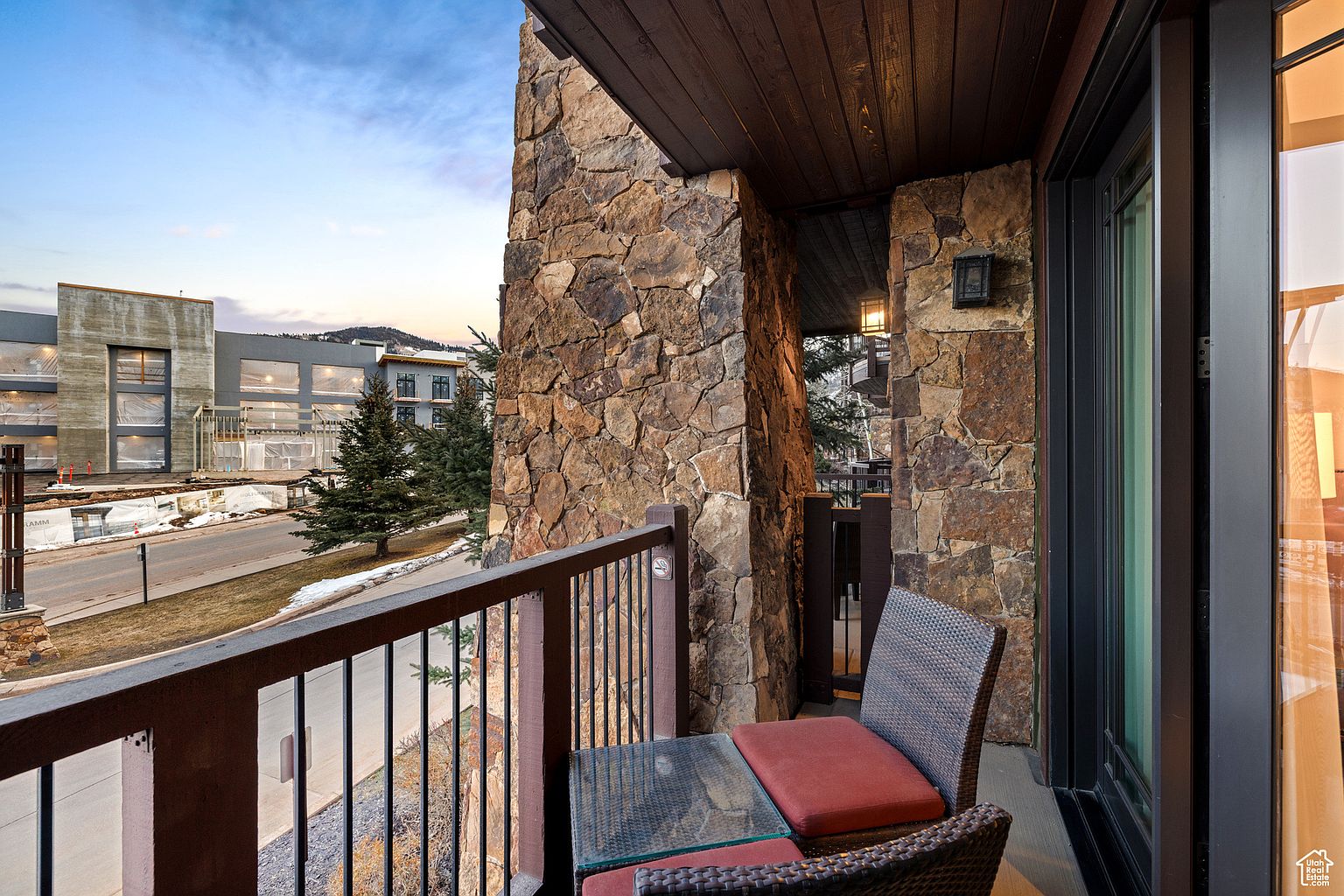 This image showcases a cozy balcony with a stone facade, offering a private outdoor space. The balcony features a small table and chairs with red cushions, perfect for enjoying the view. The railing provides a sense of enclosure while still allowing for an open view of the surrounding landscape and nearby buildings.