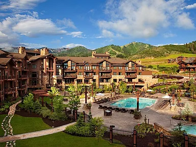 This image showcases an inviting outdoor pool and spa area situated within a luxurious residential complex. The neatly manicured landscaping, including vibrant greenery and stone pathways, complements the building's architecture and creates a resort-like atmosphere. Mountain views in the background enhance the property's appeal and offer a sense of tranquility and escape.