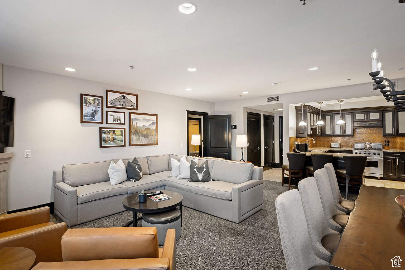 This interior shot showcases a well-lit living room that seamlessly transitions into a modern kitchen. The living area features a comfortable sectional sofa, complemented by stylish artwork and a round coffee table. The kitchen boasts dark cabinetry, granite countertops, and stainless steel appliances, creating a sophisticated and inviting atmosphere.