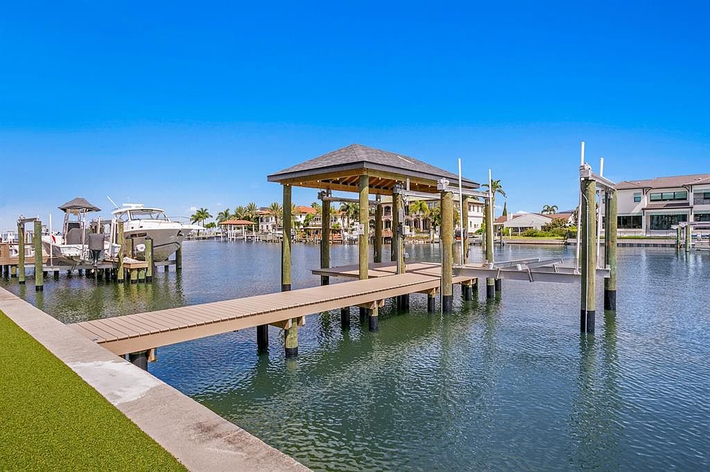 This image showcases a waterfront property with a private dock and boat lift. The dock features a covered area, providing shade and shelter. A boat is moored nearby, and luxurious waterfront homes are visible in the background, creating an impression of upscale coastal living.