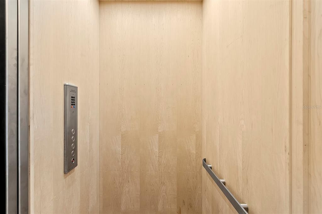 The image showcases the interior of an elevator, featuring light wood paneling on the walls and a stainless steel control panel with buttons. A handrail is visible on the right side, adding a touch of safety and accessibility. The overall impression is clean, modern, and functional.