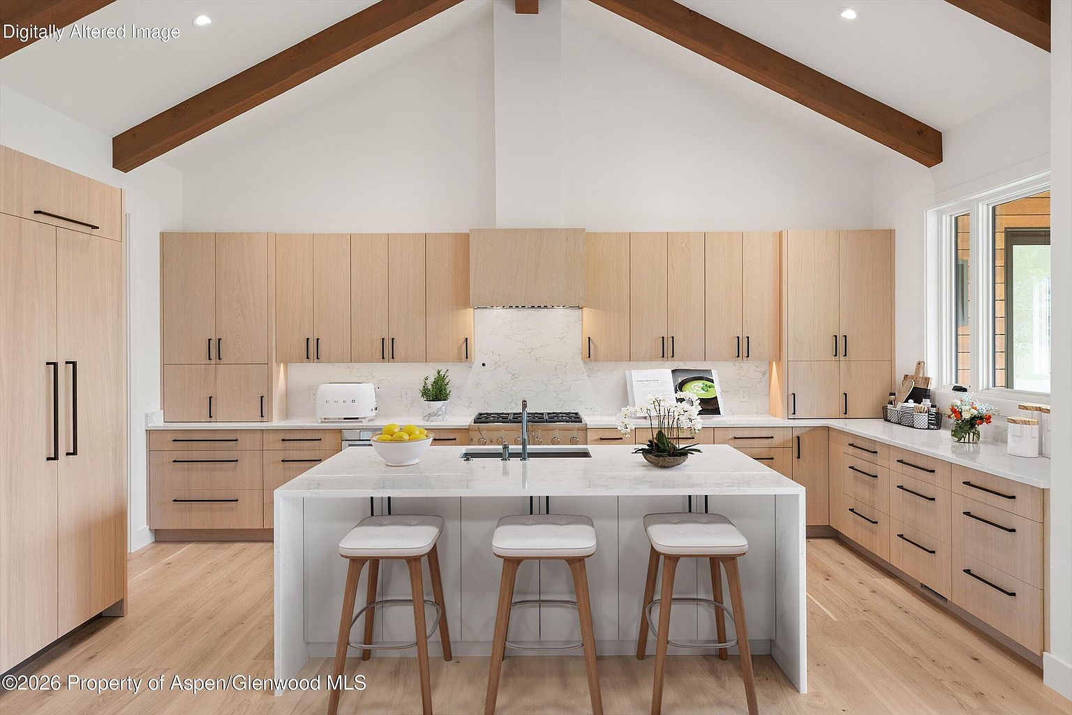 This bright, modern kitchen features light wood cabinetry, a large central island with a stone countertop, and three bar stools. The space is defined by a high vaulted ceiling with exposed wooden beams and a clean, minimalist aesthetic. A marble-patterned backsplash and integrated appliances create a seamless, high-end look, while the perspective captures the entire workspace from a centered, eye-level vantage point.