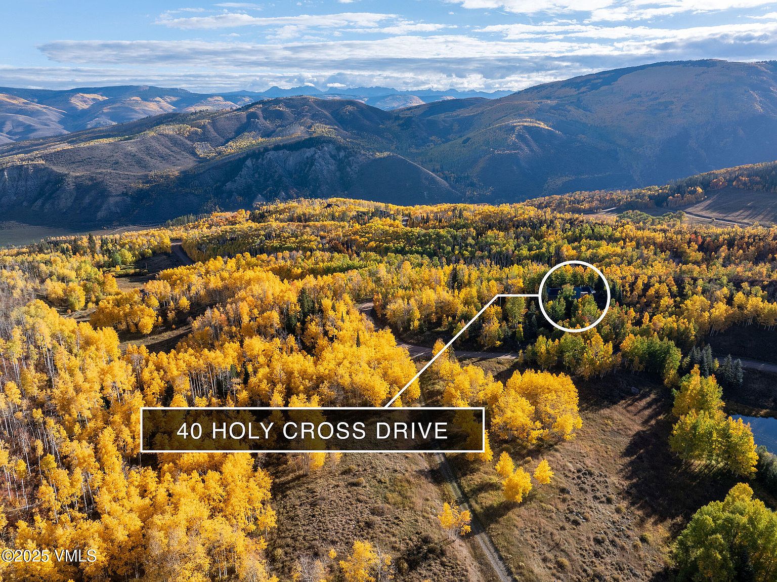 This aerial view showcases a property nestled amidst a vibrant autumn landscape. The surrounding hills are covered in trees displaying fall colors, with a house partially visible within a circle of trees. The image highlights the property's secluded location and natural beauty.
