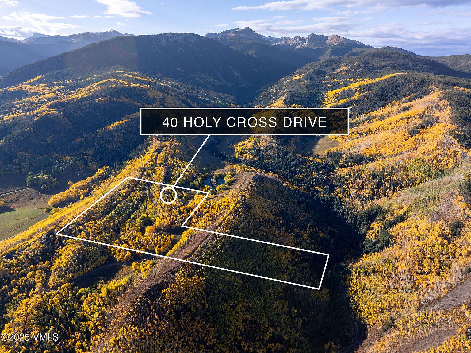 This aerial shot showcases a large property nestled in a mountainous, wooded area. The landscape is a mix of evergreen and deciduous trees, with the latter displaying vibrant fall colors. The property boundaries are outlined, highlighting the expansive land available, and a small pond adds to the natural beauty of the setting.