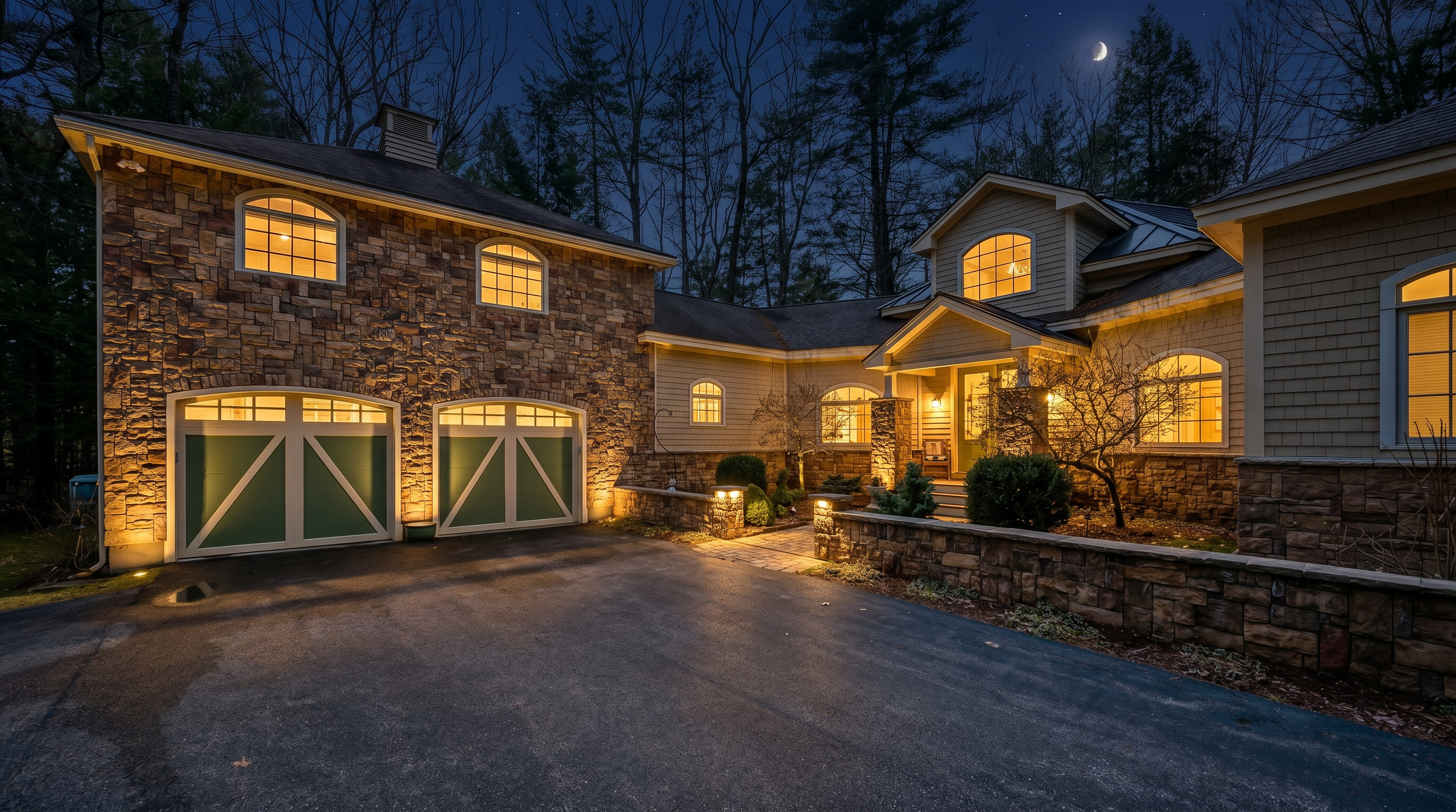 This charming suburban home features a blend of rustic stone veneer and light-colored shingle siding, creating a warm and inviting curb appeal. The property includes an attached two-car garage with distinctive green doors, a stone-walled entryway, and arched windows that add architectural character. Surrounded by mature trees, the house presents a well-maintained and picturesque facade.