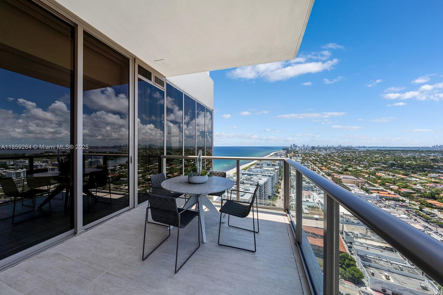 This image showcases a modern balcony with a stunning view of the ocean and city skyline. The balcony features a round table with four chairs, perfect for enjoying the scenery. The glass railing provides an unobstructed view, enhancing the appeal of this outdoor living space.