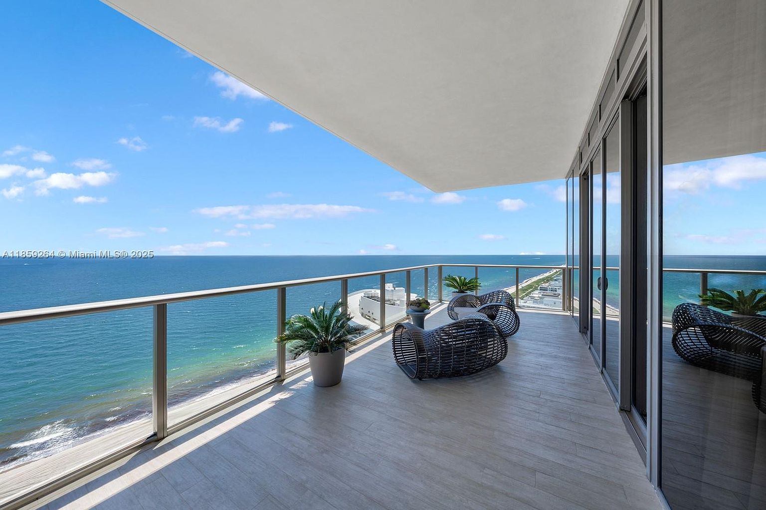 This image showcases a luxurious balcony with stunning ocean views. The balcony features modern outdoor furniture, potted plants, and a sleek glass railing. The flooring appears to be light-colored wood or tile, complementing the contemporary design of the building.