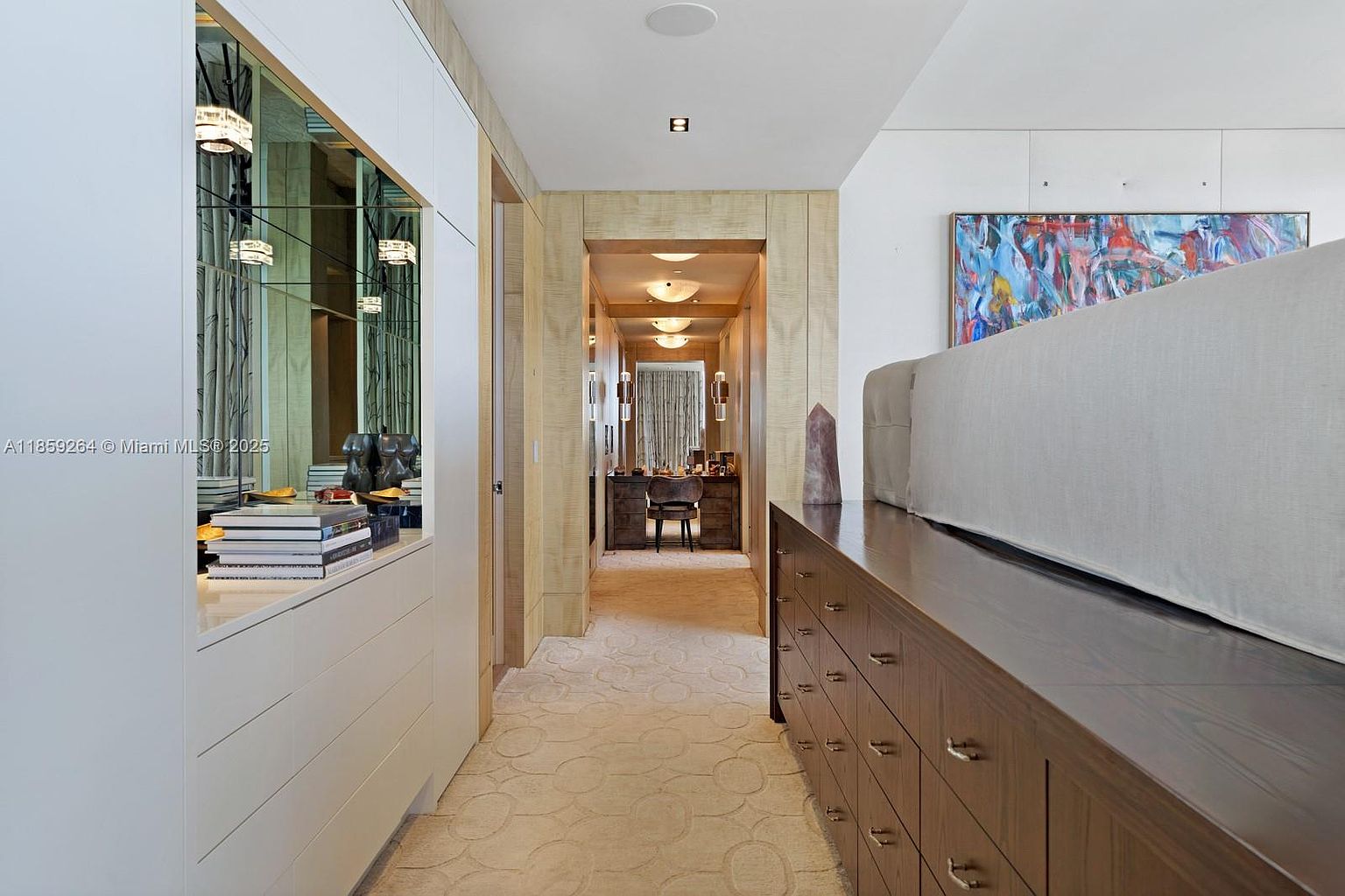 This interior shot showcases a well-lit hallway with a sophisticated design. The hallway features a patterned carpet, wood-paneled walls, and built-in cabinetry with mirrored accents. A glimpse into an office space is visible at the end of the hallway, creating a sense of depth and luxury.