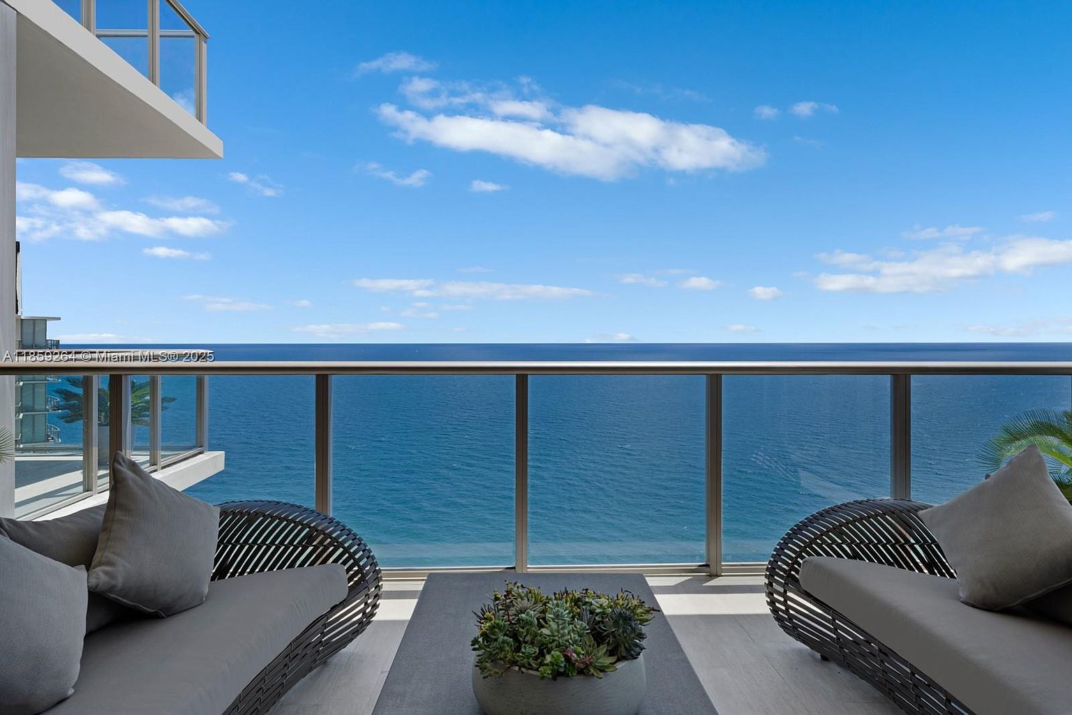 This image showcases a luxurious balcony with stunning ocean views. The balcony features modern outdoor furniture, including comfortable seating and a stylish coffee table with a succulent arrangement. The glass railing provides an unobstructed view of the ocean and sky, creating a serene and inviting outdoor living space.