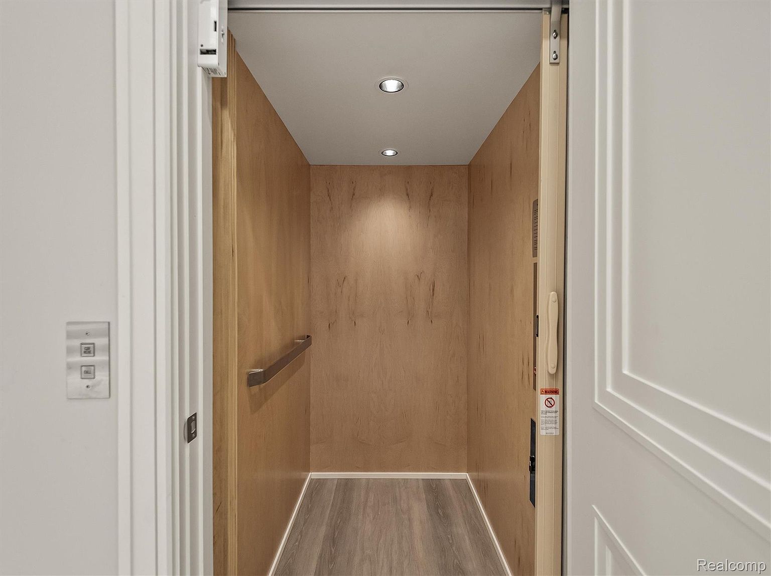 The image showcases the interior of a residential elevator. The elevator features wood-paneled walls, recessed lighting, and a handrail for accessibility. The floor is covered with wood-look planks, and the overall impression is clean and functional, suggesting a modern and convenient home amenity.