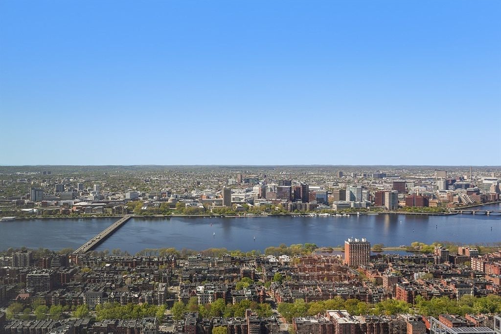 This aerial view showcases a sprawling cityscape with a prominent river running through it, crossed by multiple bridges. The buildings range from low-rise residential areas to taller commercial structures, all under a clear blue sky. The image provides a sense of the city's scale and its integration with the natural landscape.