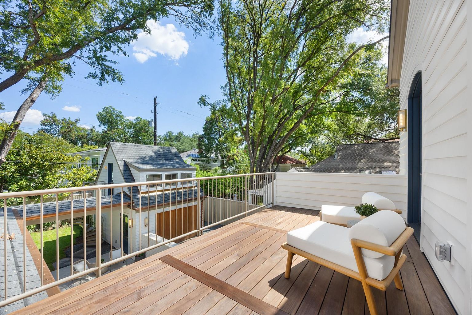This image showcases a beautifully designed outdoor deck area, featuring wooden flooring and a modern railing system. Two white lounge chairs invite relaxation, while the surrounding trees provide shade and privacy. The deck offers a serene outdoor living space, perfect for enjoying the natural surroundings.