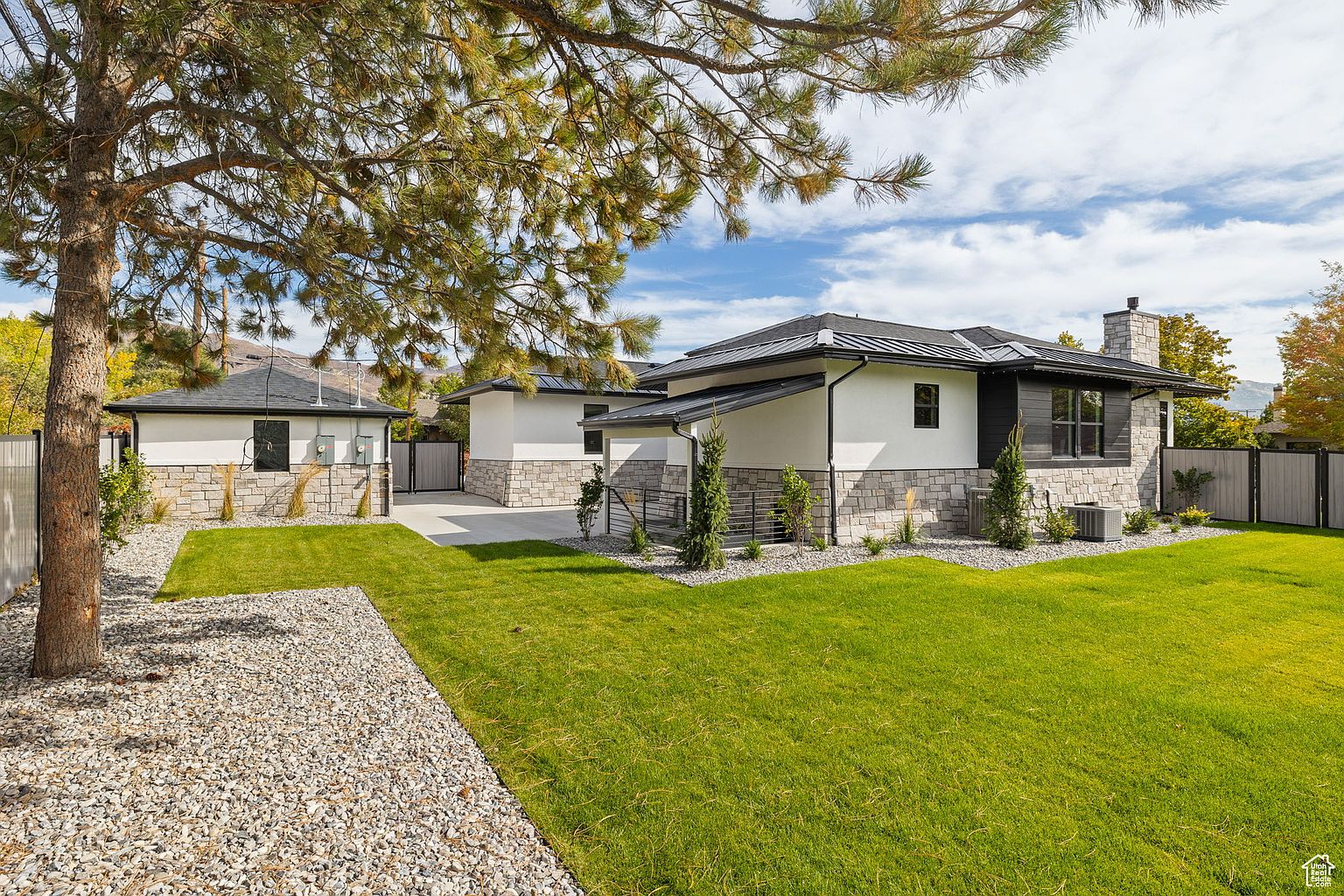 This image showcases the exterior of a modern home, emphasizing its well-maintained yard and garden. The property features a combination of stone and white siding, complemented by a lush green lawn and gravel landscaping. The overall impression is one of a meticulously cared-for and inviting outdoor space, perfect for relaxation and entertainment.