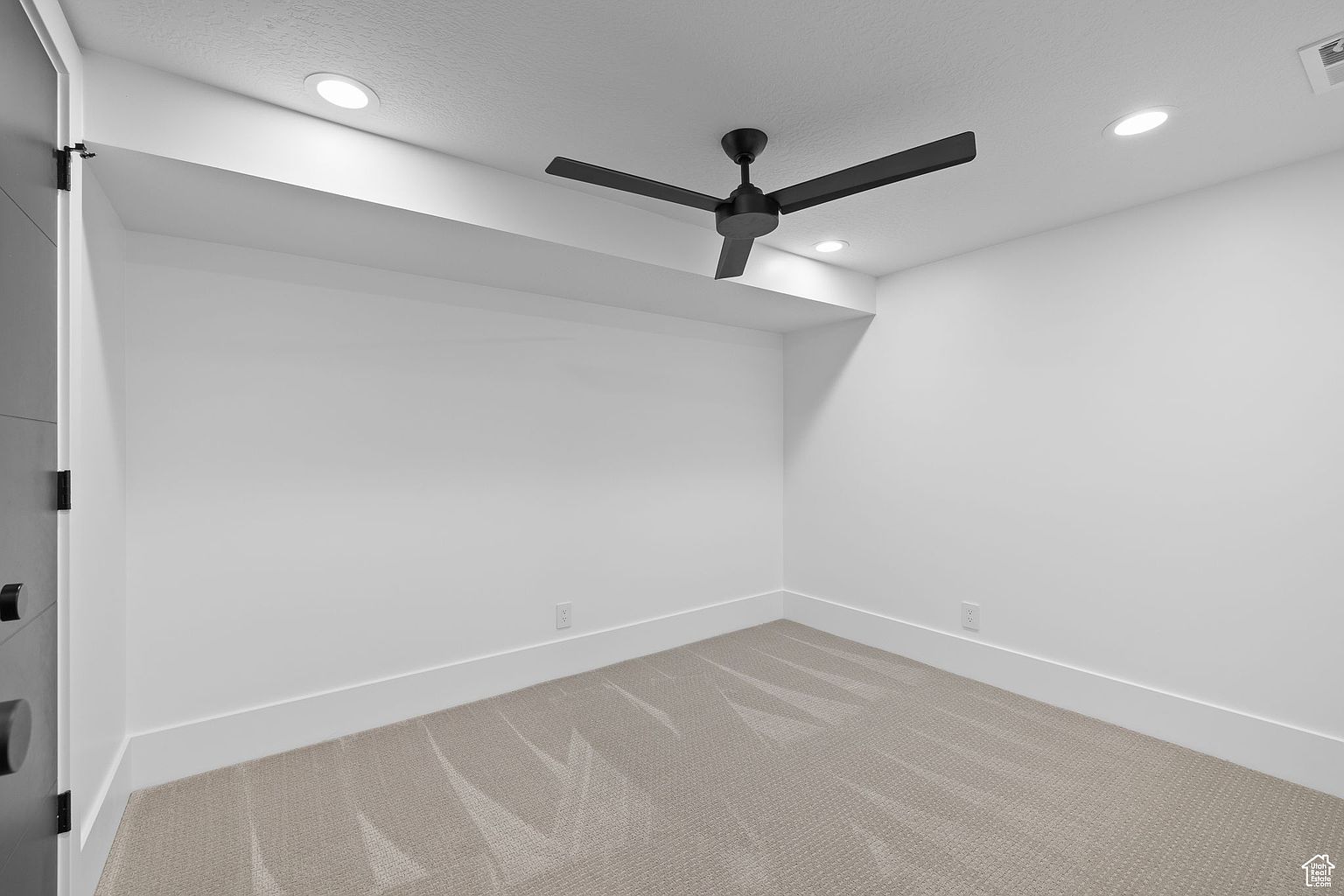 This is a clean and modern bedroom featuring neutral-toned carpet and white walls, creating a bright and airy atmosphere. A black ceiling fan adds a touch of contrast, while recessed lighting provides ample illumination. The room is simple yet elegant, offering a blank canvas for potential buyers to envision their own personal style.