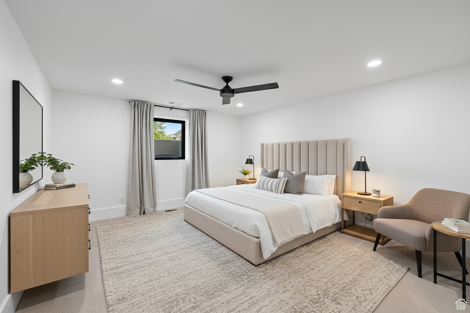 This image displays a tastefully decorated primary bedroom featuring a neutral color palette. The room includes a bed with a high, upholstered headboard, two bedside tables with lamps, and an accent chair. A dresser with a mirror is also visible. Overall, the bedroom conveys a sense of calm and sophistication.