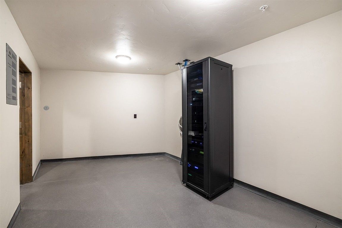 This interior shot showcases a dedicated server room, featuring a large, enclosed server rack filled with electronic equipment. The room has a clean, minimalist aesthetic with light-colored walls, a gray floor, and a simple ceiling light. The space appears well-maintained and designed for functionality.
