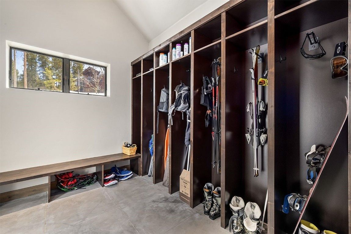 This interior shot showcases a well-organized mudroom or hallway area, featuring custom dark wood lockers for storage of outdoor gear. A long wooden bench sits beneath a window, providing a place to sit and remove shoes. The space is clean and functional, ideal for a family home in a snowy climate.