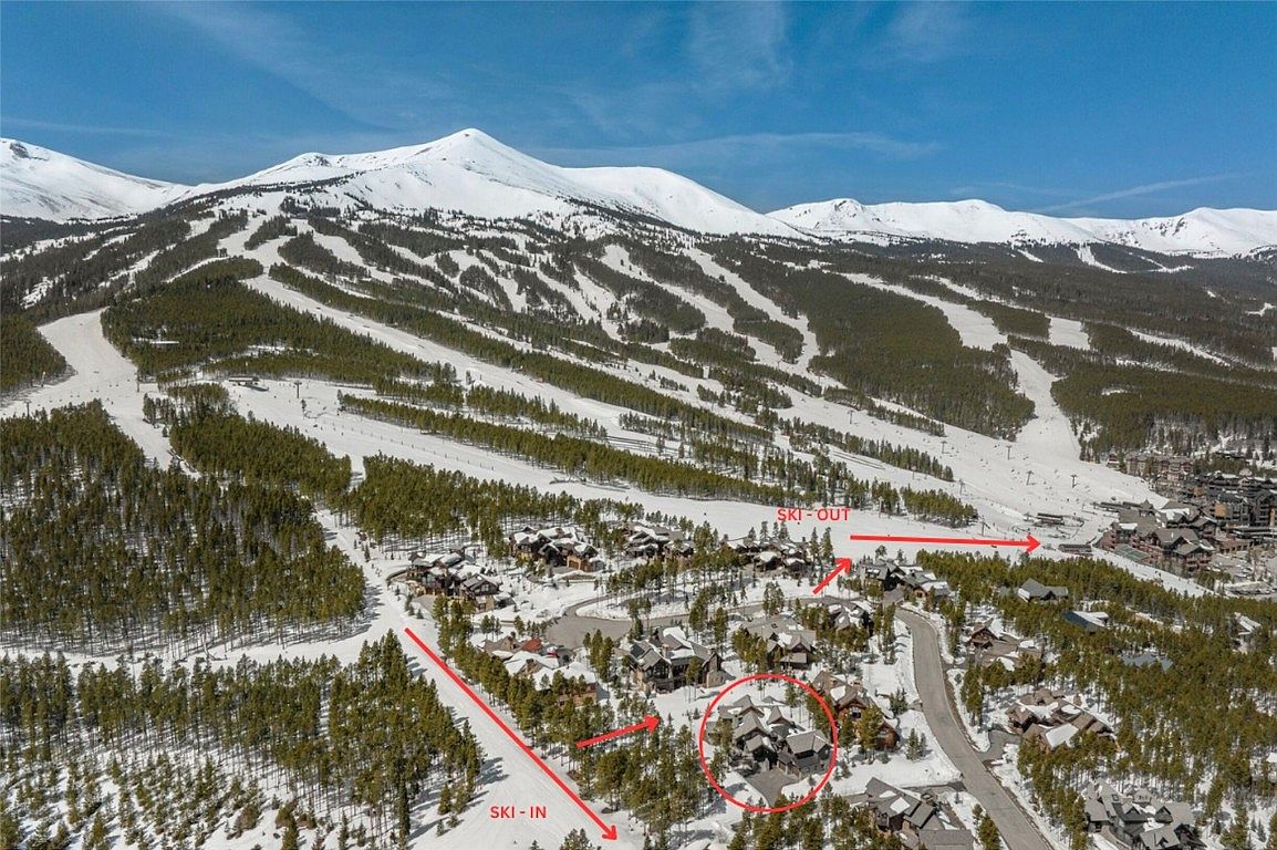 This aerial shot showcases a luxurious ski-in/ski-out property nestled in a snowy mountain landscape. The home, circled in red, is surrounded by mature trees and other upscale residences, with ski slopes visible in the background. The image emphasizes the property's prime location and access to winter recreational activities.