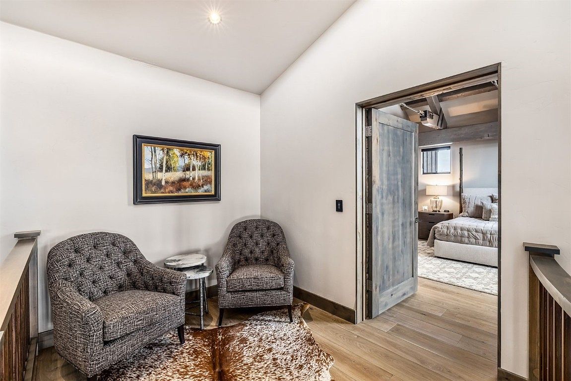 This interior shot showcases a cozy hallway leading into a bedroom. The hallway features two armchairs, a small side table, and a cowhide rug, creating a welcoming seating area. A framed painting hangs on the wall, and a partially open wooden door reveals a glimpse of the bedroom with a bed and nightstand, suggesting a comfortable and private space.