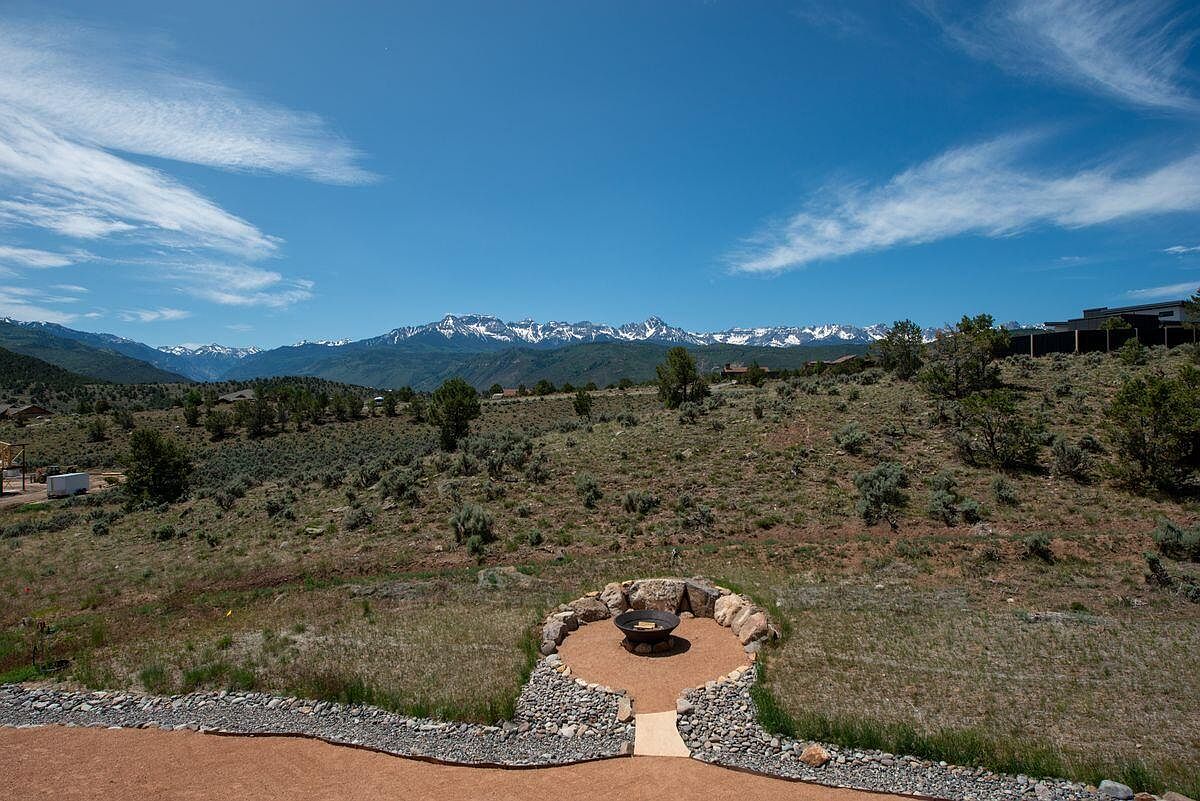 This image showcases a beautifully landscaped yard with a fire pit area as a focal point. The fire pit is surrounded by a stone seating area, creating an inviting outdoor space. The yard features natural vegetation and offers stunning mountain views in the background, enhancing the property's appeal.