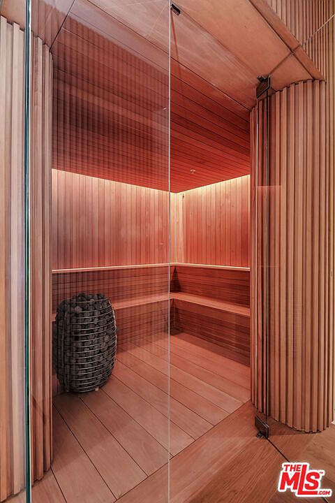 This image showcases a sleek, modern sauna featuring warm-toned wood paneling and integrated ambient lighting. A glass door provides a clear view into the minimalist interior, which includes tiered wooden benches and a cylindrical stone heater. The design emphasizes a luxurious, spa-like atmosphere perfect for relaxation.