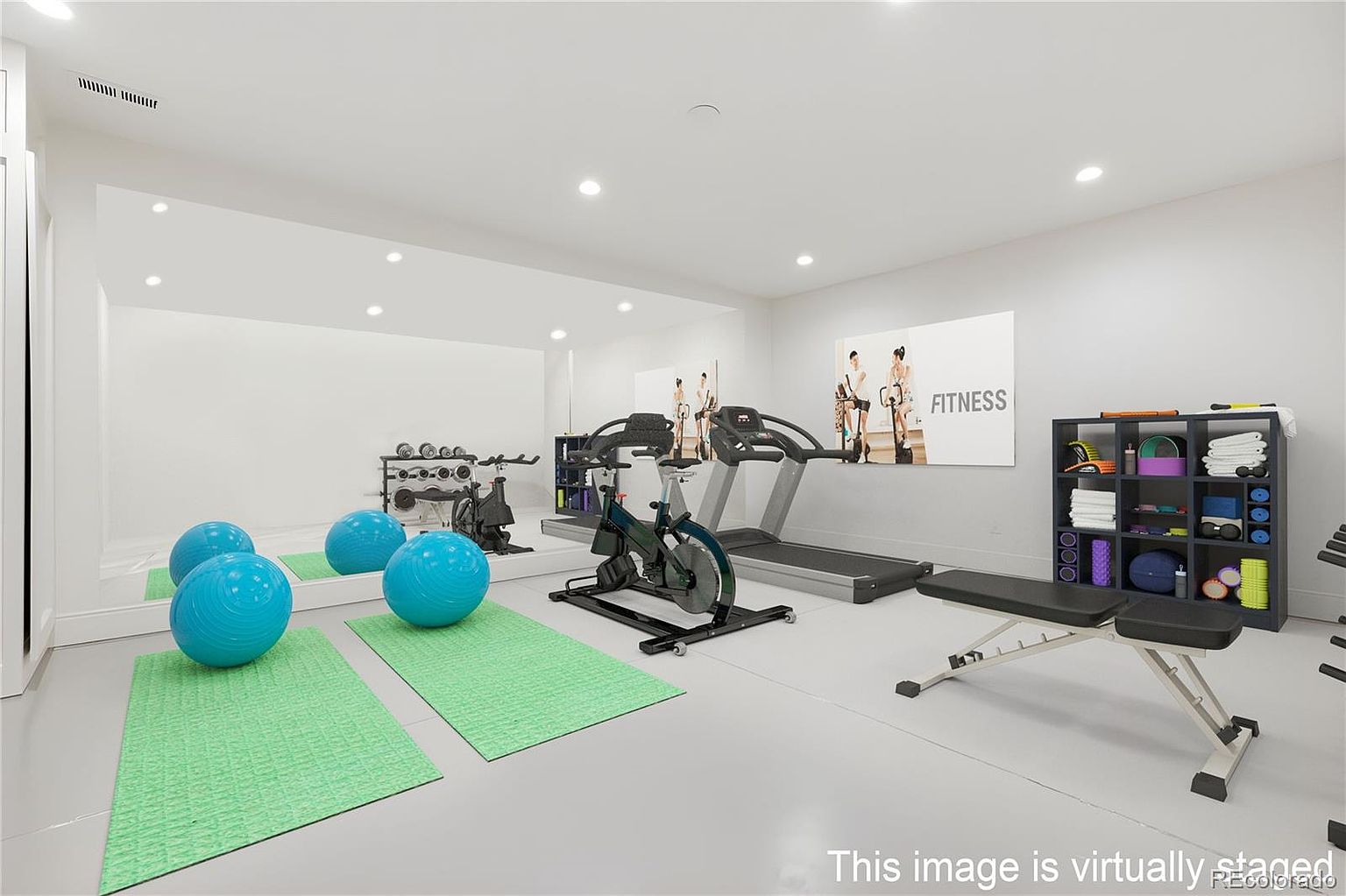 This is an interior shot of a home gym. The room features exercise equipment such as a treadmill, stationary bike, weight rack, and exercise balls. The walls are painted white, and there is a large mirror on one wall, creating a bright and spacious feel.
