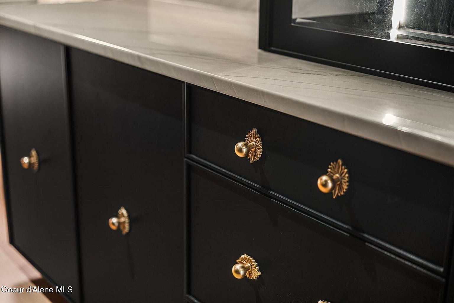 The image showcases a close-up of a black cabinet or dresser with ornate gold hardware. The countertop is a light marble or quartz, adding a touch of luxury. The focus is on the elegant design and high-end finishes, highlighting the quality of the furniture.