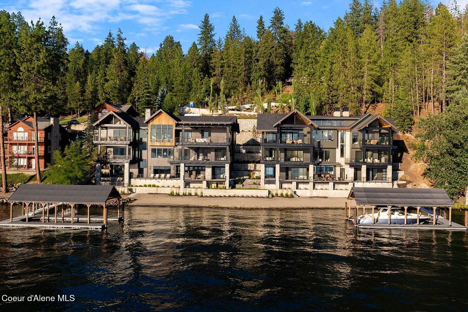 This image showcases the rear exterior of a luxurious waterfront property, featuring multiple levels with balconies and expansive windows offering stunning views. The architecture is modern and sophisticated, complemented by well-maintained landscaping and private boat docks. The property is nestled against a backdrop of lush, mature trees, enhancing its privacy and appeal.