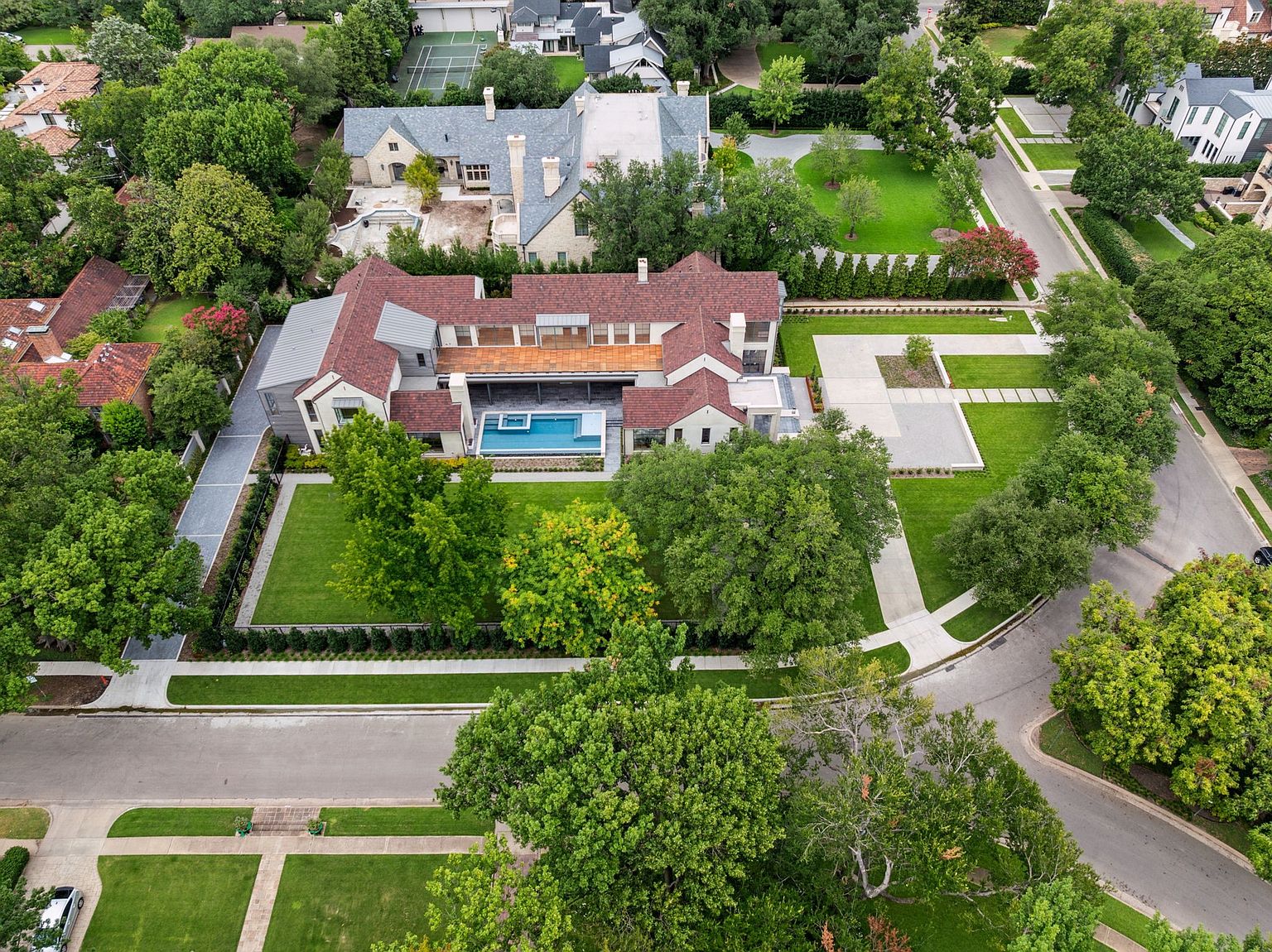 This aerial view showcases a luxurious estate with meticulously manicured grounds. The property features a large house with a red-tiled roof, a swimming pool, and a formal garden area. The surrounding landscape includes mature trees and well-maintained lawns, creating a sense of privacy and elegance.